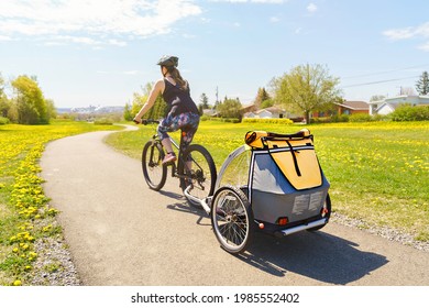 A woman riding a bicycle with a baby stroller attached to the bicycle.