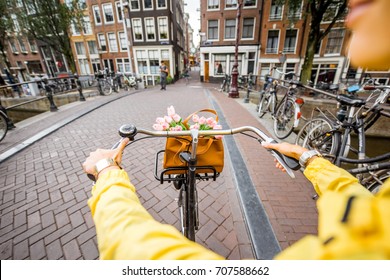 Woman riding a bicycle with bouquet of flowers on the street in Amsterdam city. View on the hands holding helm
