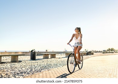 Woman Riding Bicycle On Beach Promenade In Summer. Happy Lady On Bike Having Fun On Seaside Boulevard. Sunny Waterfront Street For Cycling. Blue Sky, Summertime Freedom. Carefree Feeling At Sunset.