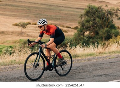 Woman riding a bicycle on empty road. Sportswoman in fitnesswear practicing on pro bike. - Shutterstock ID 2154261547