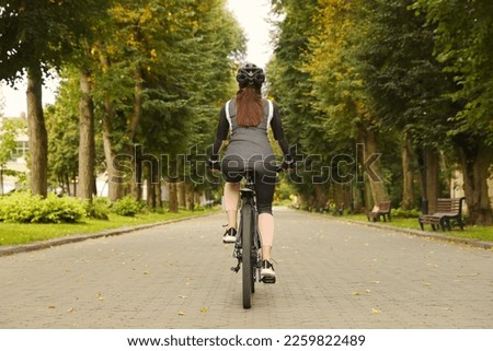 Woman riding bicycle on road outdoors, back view