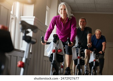 Woman, riding and bike at gym with earphone for fitness, training and workout listening to music for balance. Mature people, cycling machine and spin class exercise, wellness or cardio health goal - Powered by Shutterstock