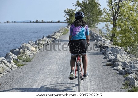 woman riding bike on gravel trail (young south asian, indian rider on bicycle trail) burlington vermont colchester causeway path (brown skin, athletic clothes, cycling jersey, helmet)
