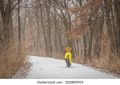 Woman Riding Her Bicycle On Park Trail In Blizzard In Midwest; Bare Trees On Both Sides