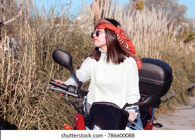 The woman riding the motorcycle. She has a bandana and sunglasses.