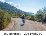 Woman riding MTB in Maremma nature reserve, Tuscany, Italy. Cycling among extensive pine forest olive trees and green woodland in natural park, dramatic coast