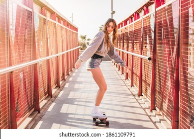 Woman riding a skateboard on a bridge in Barcelona. Skater girl on a longboard. Cool female skateboarder at sunset.
