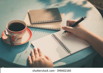 Woman right hand writing journal on small notebook at outdoor area in cafe with morning scene and vintage filter effect - Shutterstock ID 398402185