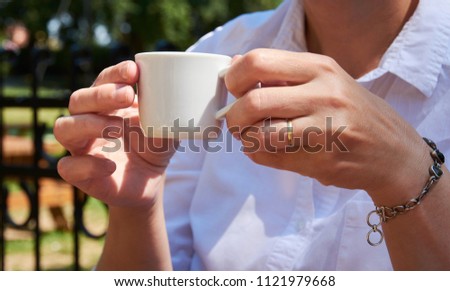 Woman with a ring on her hands holding a white cup of coffee in a garden on a sunny summer day