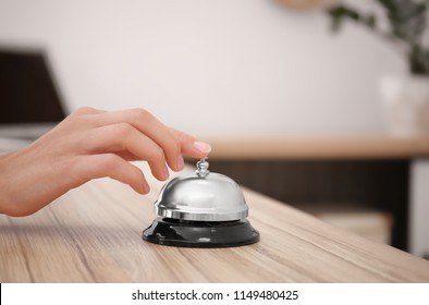 Woman ringing service bell on reception desk in hotel, closeup
