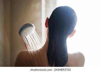 A woman rinses long hair under taking a shower, back turned, with sunlight enhancing the water's clarity.  Skin care and hygiene concept. - Powered by Shutterstock