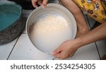 A woman is rinsing rice in a metal bowl filled with water. The woman