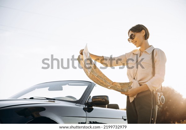 Woman\
road tripping by cabriolet and looking at the\
map