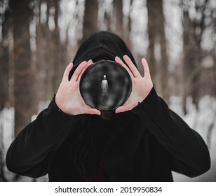 a woman in a robe covers her face with a black obsidian mirror in which a ghost can be seen - Shutterstock ID 2019950834