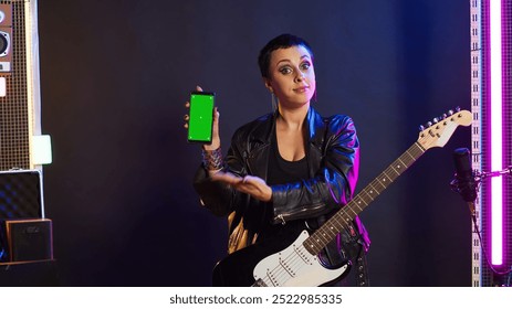 Woman rock musician playing guitar next to green screen display on device, doing a live music performance on stage at the nightclub. Artist rocker acting cool and rebellious with edgy style. Camera A. - Powered by Shutterstock