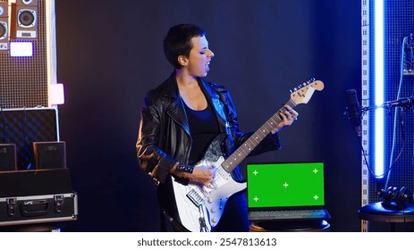 Woman rock performer playing bass guitar next to mockup display on device, doing a live music performance on stage at the nightclub. Artist acting cool and rebellious with edgy style. Camera A. - Powered by Shutterstock