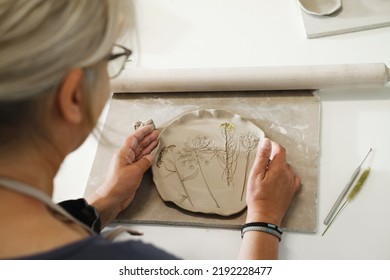 Woman rolling clay, making ceramic plate in studio with floral pattern. Handmade creative work. Pottery workshop for adults. Top view on plate - Shutterstock ID 2192228477