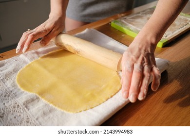 A woman rolls out the dough with a rolling pin with her hands for a delicious cake on a wooden table background on a sunny warm day.