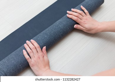 woman rolls a rubber yoga mat on the studio floor. Only her hands are visible. - Shutterstock ID 1132282427