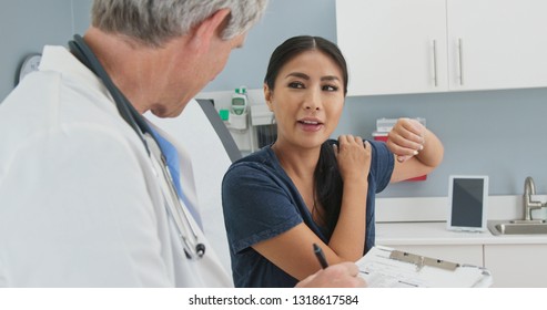 Woman With Rotator Cuff Injury Listening To Doctor Explain Treatment Options. Japanese Patient  And Caucasian Doctor Talk About Dislocated Shoulder Pain