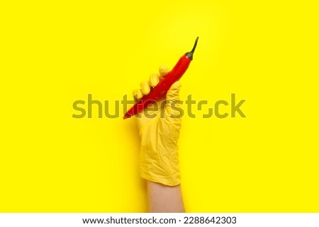 Woman in rubber glove with chili pepper on yellow background