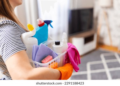 Woman in rubber gloves with basket of cleaning supplies ready to clean up