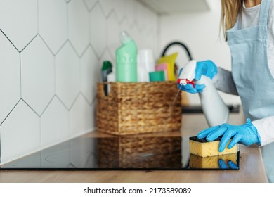 Woman in rubber gloves clean glass ceramic surface on induction stove, polish kitchen with sponge, using eco friendly spray. Housewife doing daily household routine. Housekeeping services concept