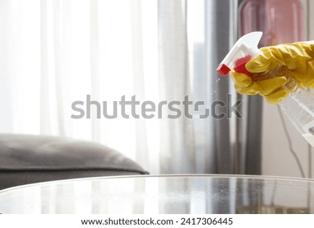 Woman in rubber gloves cleans a coffee table with a spray. Spraying and wiping glass table.	