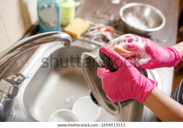 Woman in rubber gloves washing up dishes and pot.\
Stay home clean house
