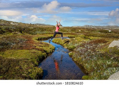 Woman run free jumping little meandering stream in high country of Australia