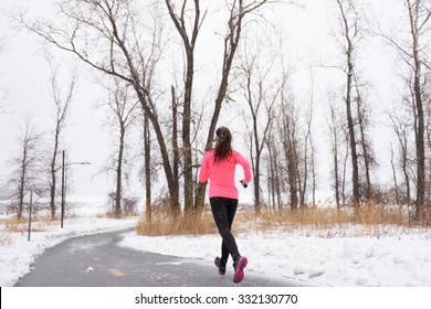 Woman Runner Running In Winter Snow - Active Lifestyle. Female Athlete From The Back Jogging Training Her Cardio On City Park Path Outside In Cold Weather Wearing Leggings And Coat.