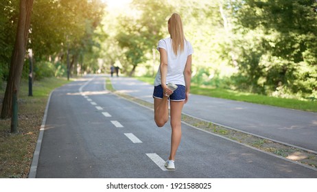 Woman runner stretching legs before exercising summer park  morning Middle age athletic female warming up body before running Caucasian person warm up jogging Dressed white shirt shorts running track
