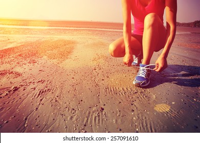 woman runner tying shoelace before running on beach