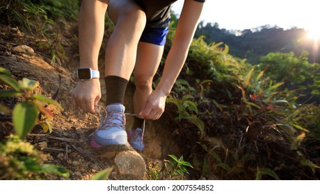 Woman runner tying shoelace on mountain trail - Powered by Shutterstock