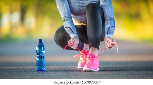 Woman Runner Tying Shoelaces Before Jogging In Autumn Tree Alley Park. Sports Female Autumn Outfit Leggings And Thermal Underwear. Sports Drinking Regime Concept.