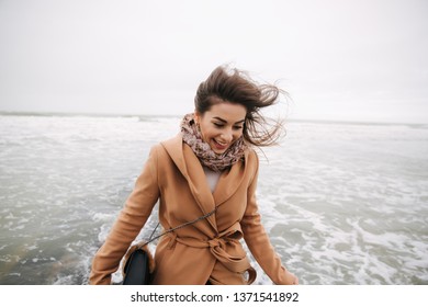 Woman Running Away From The Waves Of North Sea. Female Afraid To Be Wet In Cold Weather