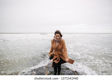 Woman Running Away From The Waves Of North Sea. Female Afraid To Be Wet In Cold Weather