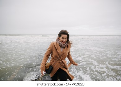 Woman Running Away From The Waves Of North Sea. Female Afraid To Be Wet In Cold Weather