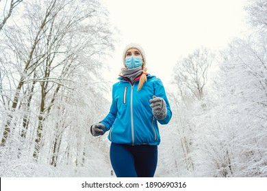 Woman running or jogging with face mask in the covid-19 winter during snowy landscape