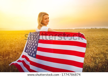 Woman running and jumping carefree with open arms over wheat field Holding USA flag.