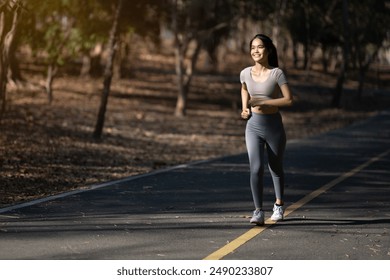 A woman is running on a road with trees in the background. She is smiling and she is enjoying her run - Powered by Shutterstock