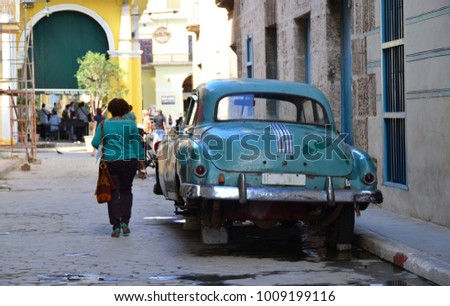 Woman is running past a jacked-up vintage car, Havana, Kuba