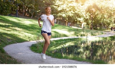 Woman running road summer park near lake Active sporty caucasian female morning workout Healthy lifestyle concept. Athletic person sportswear exercises Dressed white t-shirt full length