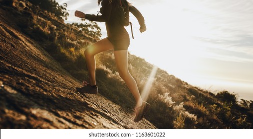 Woman running up a rocky mountain slope. Cropped shot of female trail runner running uphill on a sunny day.