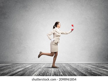 Woman Running In Room With Vintage Red Phone. Call Center Operator In White Business Suit Posing With Telephone. Hotline Telemarketing And Communication. Professional Business Assistance And Support