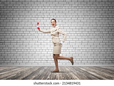 Woman Running In Room With Vintage Red Phone. Call Center Operator In White Business Suit Posing With Telephone. Hotline Telemarketing And Communication. Professional Business Assistance And Support