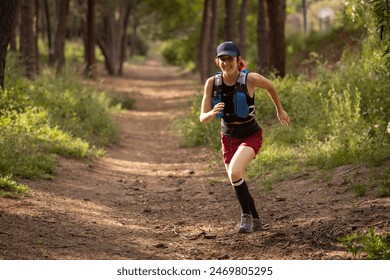 A woman is running through a forest trail. She is wearing a black shirt and red shorts. She is wearing a hat and carrying a backpack - Powered by Shutterstock