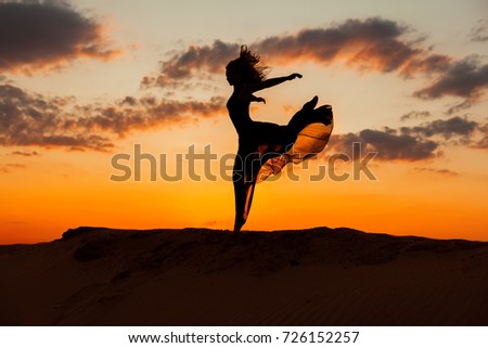 Woman runs along the barkhans against the backdrop of the setting sun.