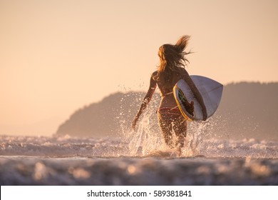 Woman runs into the ocean with surfboard