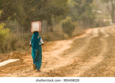A woman in rural India carrying a bag on her head.